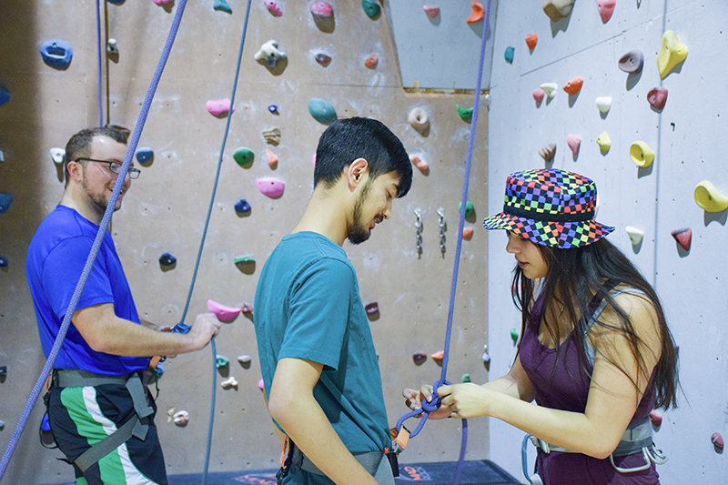 Sayuz Shrestha from Nepal (center) gets ready to climb the Northwest College Cabre Gym rock wall Monday with the help of Kiyamani Hollow Horn Bear from Red Lodge, Montana. Climbing instructor Declan Sielaff is pictured in the background.