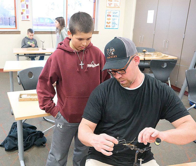 Jace Lejeuene (left) watches as Coach Eric Oram teaches him how to tie a fly.