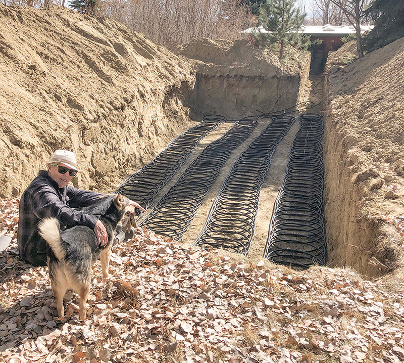 Jerry Rodriguez’s wife Susie Rodriguez sits with their dog Madchen on the edge of trench dug to house the coils for their geothermal heater.