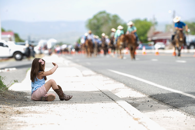 Finding a spot of shade  Kimber Moucha, 5, decked out in cowboy boots, waves to the parade of mules and riders Saturday morning.