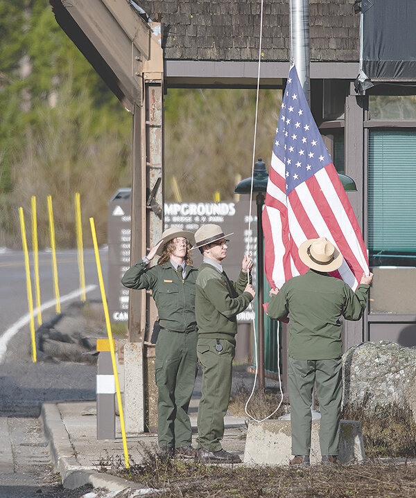 From left, Yellowstone Seasonal Recreation Fee Tech Patrick Flanagan salutes the flag as East Entrance Lead Recreation Fee employee Josh Giammichele prepares to raise the flag with the help of Chris Baltz, East Entrance fee supervisor, just prior to opening the gates to motorized vehicles Friday.