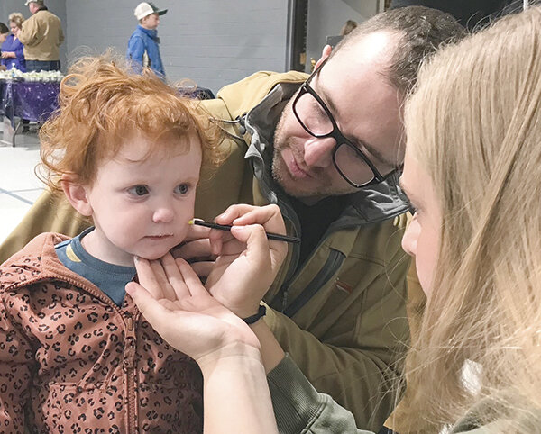 Rylee Burbank (left), gets her face painted while her father Garrett lends a helping hand at Powell Christian School’s ‘A Night with the Stars,’ April 21 in the Trinity Bible Church gym.