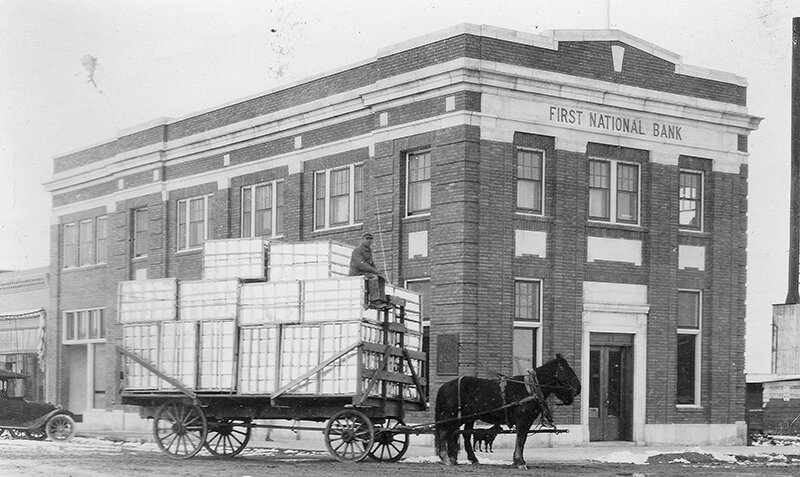 A hay wagon transports honey cans past the First National Bank building on its opening day of April 4, 1918, in a photo donated to the Homesteader Museum by Skip and Bev McCrary.