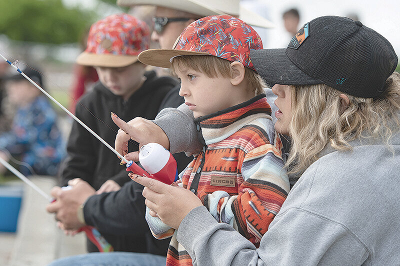 Braxton Quarles, 4, receives a fishing lesson from his mother, Senora, while his brother Hayden and grandfather, James, work together in the background during the Kids’ Fishing Day celebration Saturday at Homesteader Park.