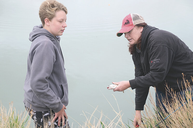 Brielle Layland (left) waits patiently while her mother Savannah Layland removes her hard earned trout from the fishing line and hands it back to her.