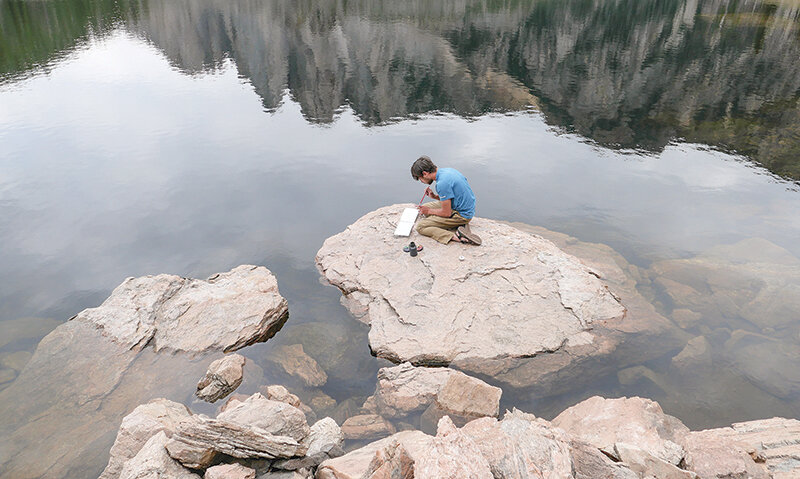 Riley Schiller, Katie Schiller’s brother-in-law and an art major at UW, perches on a rock in Deep Lake while using water colors to paint the scenery.