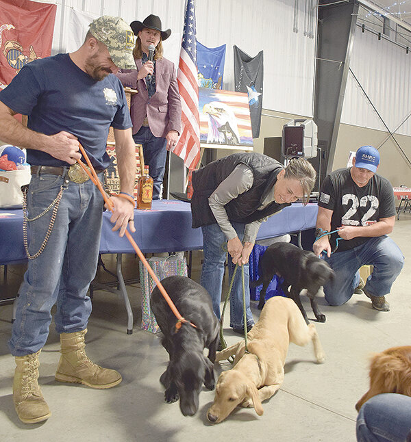Veterans Robert Cole, retired U.S. Army, Ann Williams, retired U.S. Navy, and Max Hansen, retired U.S. Navy, receive their service dogs as Sacred Mountain Retreat representative Jerrid Geving announces from the stage behind the trio and their new best friends.
