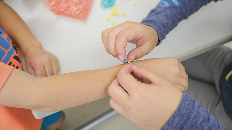 A child holds out their hand to have a beaded bracelet tied on during a Fun Friday.