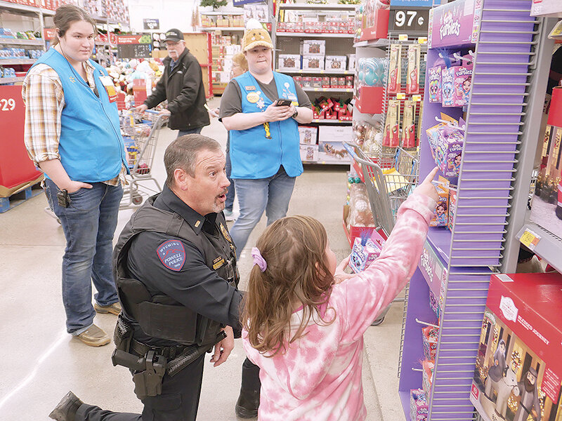Powell Police Lt. Matt McCaslin (left) and Elizabeth Nading, decided which Furby to put in the shopping cart during Shop with a Cop on Tuesday. The annual event pairs local children with law enforcement for a shopping spree at Walmart. The selected children get a shopping budget of $200-$330. Behind them are Walmart employees Kate Sorrall and Krystel Williford.