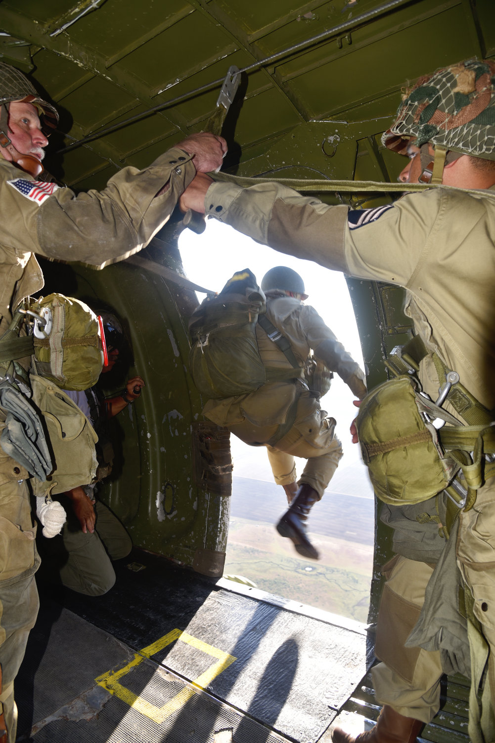 A member of the World War II Airborne Demonstration Team jumps from a World War II era C-47 called Boogie Baby. Another team member prepares to jump, while Jump Master Ken Larson keeps watch.