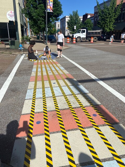 Volunteers put tape down over the guitar strings over the existing crosswalk that was painted last year before touch-up painting is done on that crosswalk on June 7, 2024.
