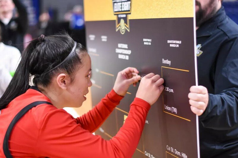 Union guard Jazalyn Anousinh puts Union's name on the semifinal bracket of a graphic with the tournament schedule at the arena for the NCAA Division II Women's Basketball National Championship tournament after Union won its first-ever quarterfinal game over Bentley.