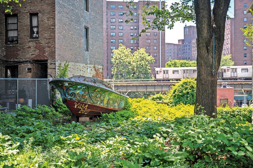 A northbound 1 train passes behind a decorative boat in a garden along Marble Hill Ave on Wednesday, June 29, 2022.
