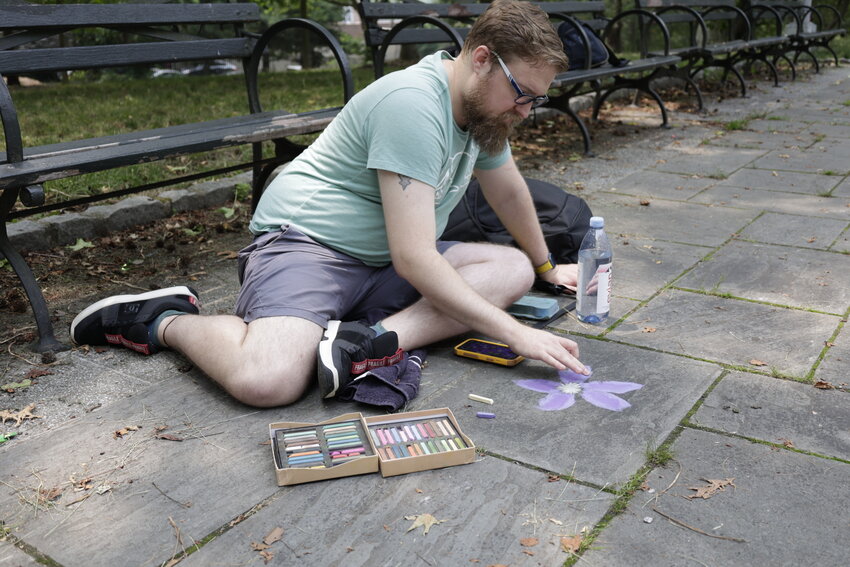 Joshua Brosz draws a flower in Henry Hudson Park on Friday, June 30, 2023. He first started messages in chalk during Covid April 2, 2020, in an attempt to spread positivity.