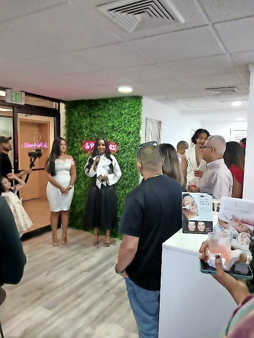Eliana Gutierrez, at left, the owner of Eliana Gutierrez Aesthetics, greets people at her Sept. 17 grand opening at the new shop while friend Zuleika Viera, holding the microphone, makes announcement. The spa is at 5676 Riverdale Ave., Suite 102. Besides a ribbon cutting, there was an open bar.
