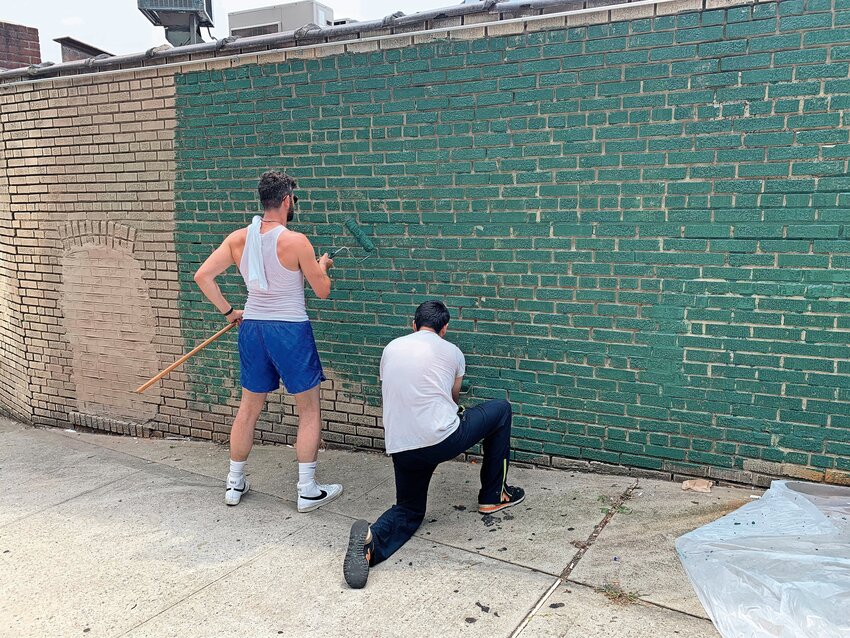 Riverdale native and artist Ian Sullivan, left, lays down the base layer for a new mural that will commemorate the Friendly Fridge&rsquo;s enduring success.