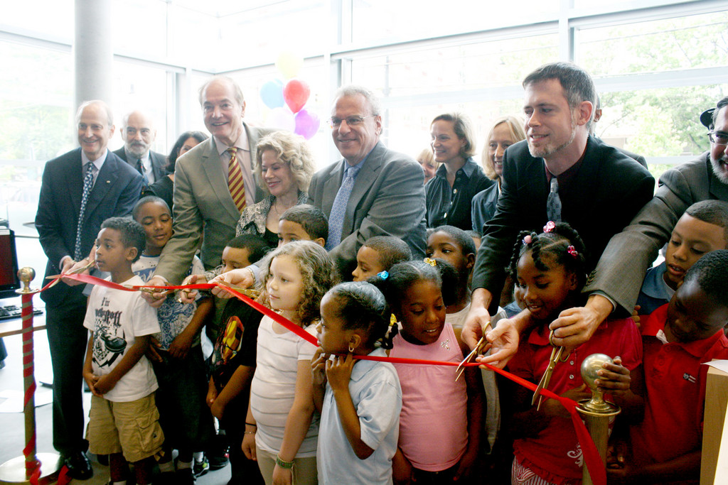 A group of distinguished guests and speakers, including state assemblyman Jeffrey Dinowitz, center, and first graders from the neighboring P.S. 37, cut the ribbon at the grand opening of the new Kingsbridge Public Library.