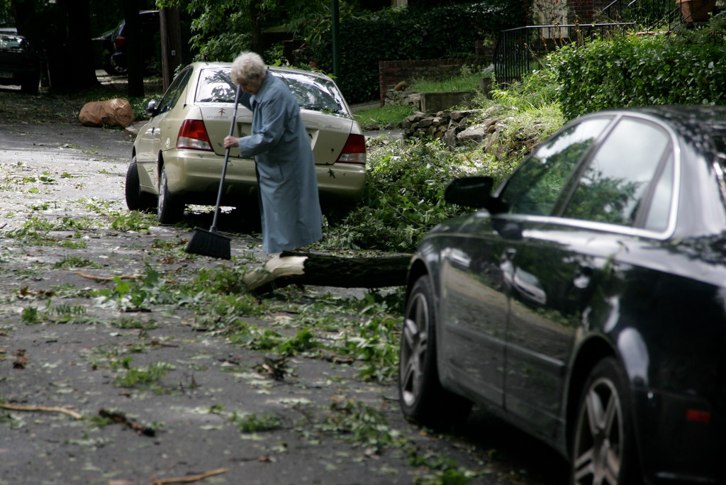 An elderly woman sweeps away the branches outside of her house.