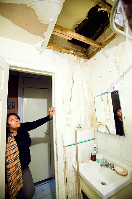 Raysette Mercedes looks up at the hole in the bathroom-ceiling 2241 Creston Ave., which is also in receivership under supervision from Howard Vargas. She says she can see the upstairs apartment. that water leaks from the hole and that rats and roaches routinely emerge through it. She says her bathroom has been this way for six months.