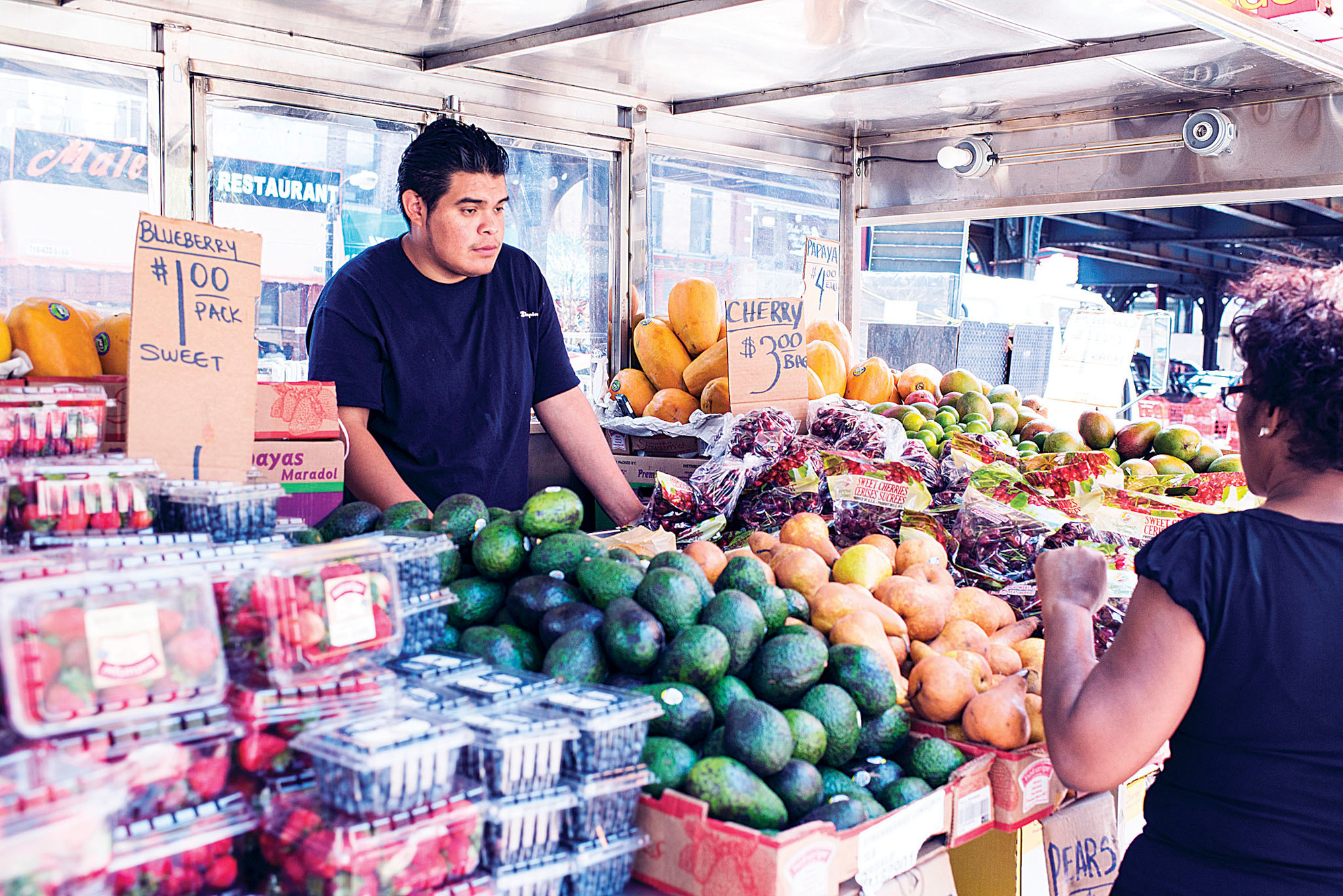 Vendor Rogelio Espinoza, 25, sells fruit to Luisa Ortiz, 40, on July 16 near Broadway and West 231st Street.