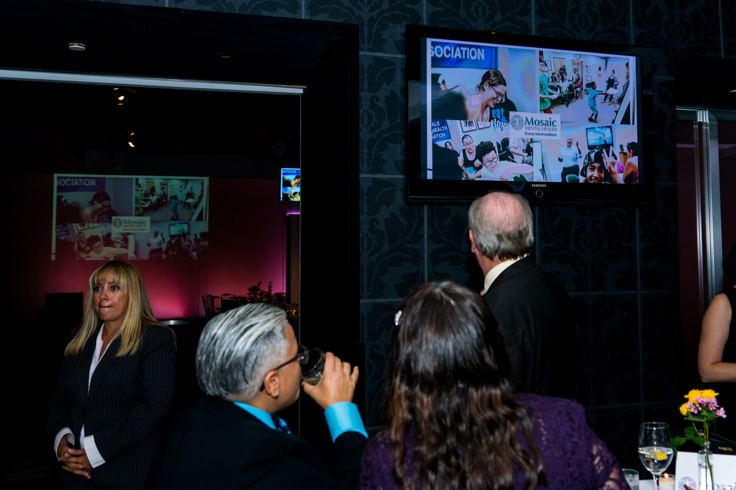 Gala attendees look at a slideshow about Mosaic Mental Health. The organization offers services like counseling and youth programs, serving 1,000 patients annually.