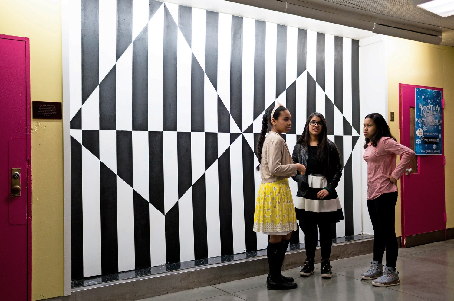 M.S. 244 students Mariam Alberto, Sherlyn Munez and Sily Netapongot talk in front of a reproduction of a painting by Carmen Herrera. They worked with other classmates and the organization Publicolor to bring the painting to life.