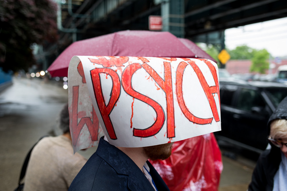A man wears a sign on his head to guard against the rain during a rally against New York-Presbyterian’s plan to decertify 30 beds in the psychiatric ward of the Allen Hospital off Broadway, just south of Marble Hill.