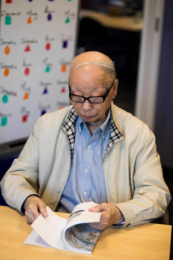 Ming Chin looks through a book of his late wife’s paintings at Riverdale Senior Services. Chin, who celebrated his 100th birthday Aug. 27, raised two children and attends the adult day program for early memory loss at RSS nearly every week.