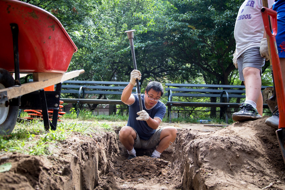 Xin Ye, a volunteer with the Stewards of Henry Hudson Park, uses a hoe to loosen soil in a plant bed at the park.