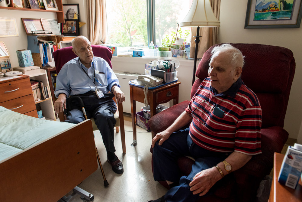 Jerry Schneider, a 92-year-old volunteer at the Hebrew Home at Riverdale, left, visits his 87-year-old friend David Oscar. Schneider reads newspapers and books to Oscar, who has problems seeing.