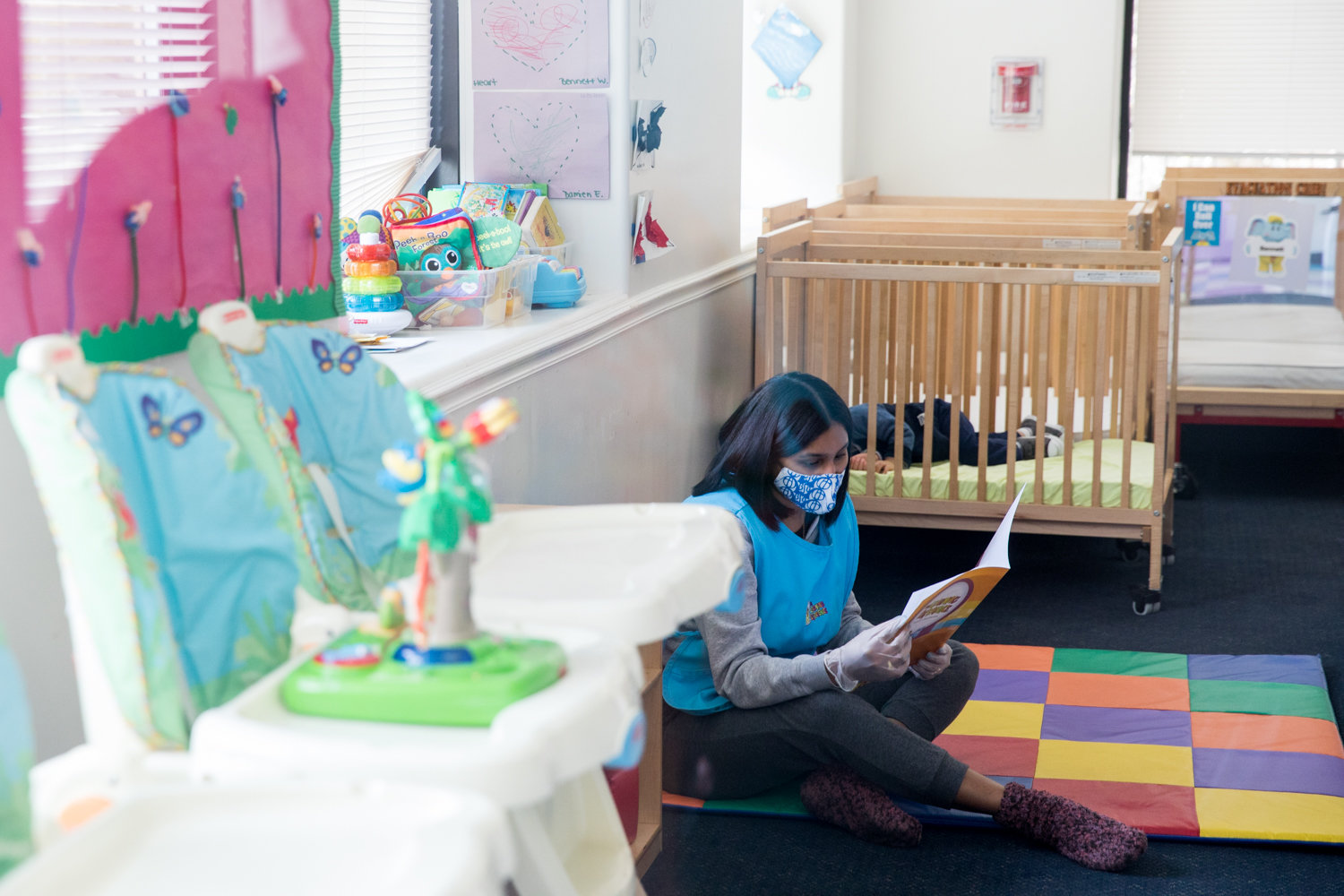 Lipsy Garcia, a teacher at The Learning Experience, looks through a book while children take a nap. The early childhood education center has retooled its services to provide day care for the children of essential workers during the coronavirus pandemic.