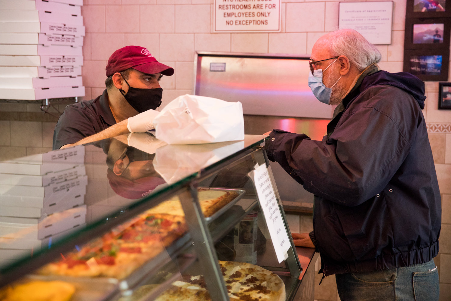Jody DePasquale, manager of Addeo’s Riverdale Pizza, left, talks with a customer while filling his order. The North Riverdale pizza place has met the challenge posed by the coronavirus pandemic, managing to stay open. DePasquale and his workers have gone to greater lengths to help the community by running errands for customers.