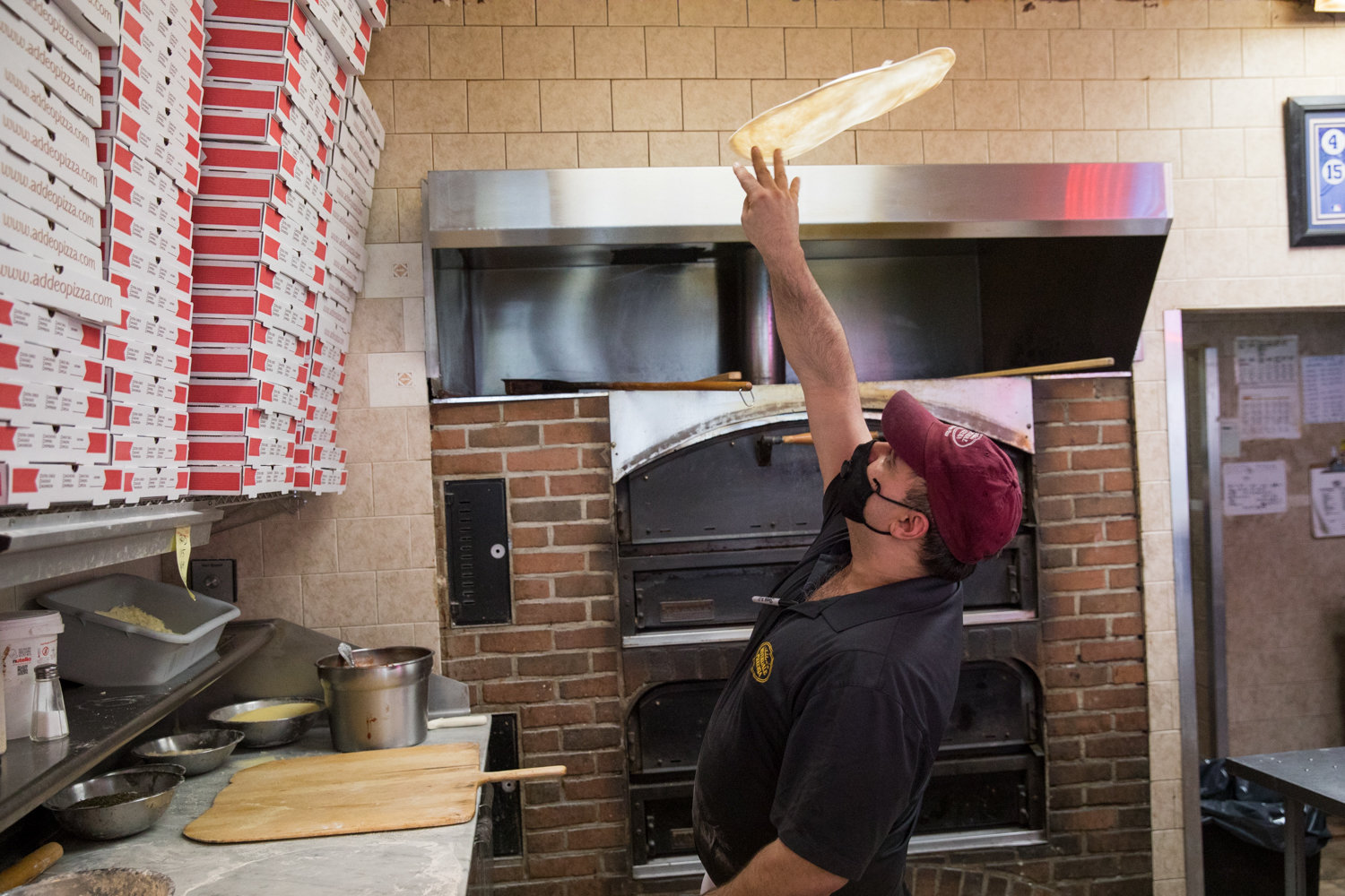 Jody DePasquale, manager of Addeo’s Riverdale Pizza, tosses dough for a pie shortly after opening. The North Riverdale pizza joint has managed to stay open despite the coronavirus pandemic, but the loss of revenue from the elimination of dining in meant employees had to work reduced hours.