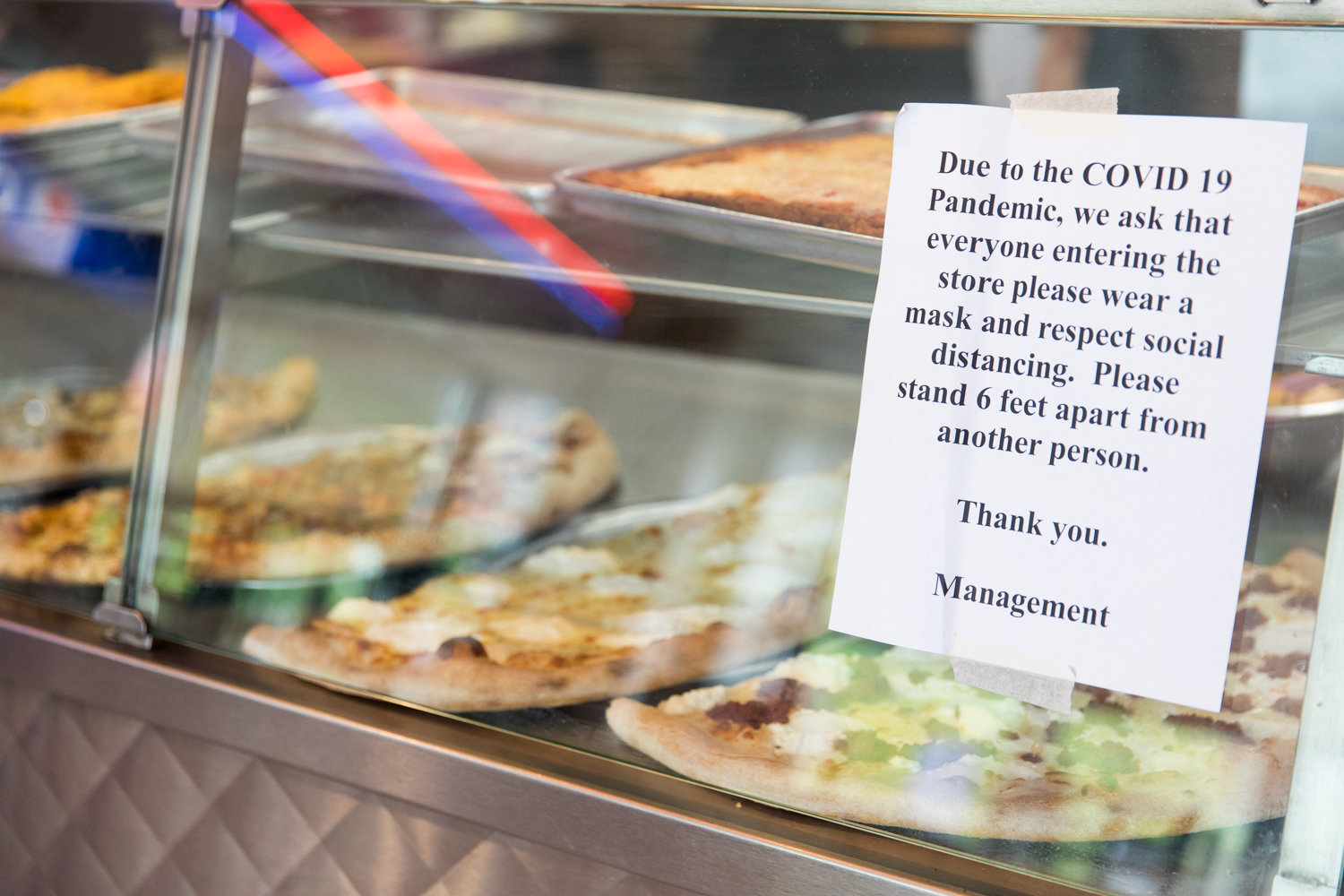 A sign posted on a display case inside Addeo’s Riverdale Pizza informs customers of the necessity of wearing a mask and keeping six feet apart, the recommended distance to help slow the spread of the coronavirus that causes COVID-19.