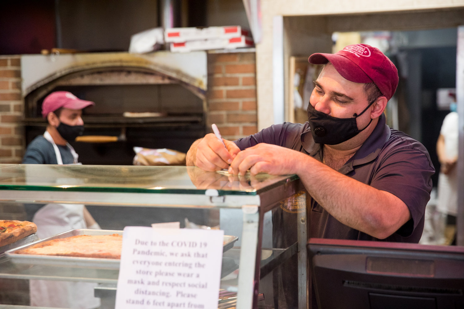 Jody DePasquale, manager of Addeo’s Riverdale Pizza, writes down a customer’s order shortly after opening. DePasquale has gone beyond his pizza-making responsibilities to help customers sequestered at home by running errands for them.