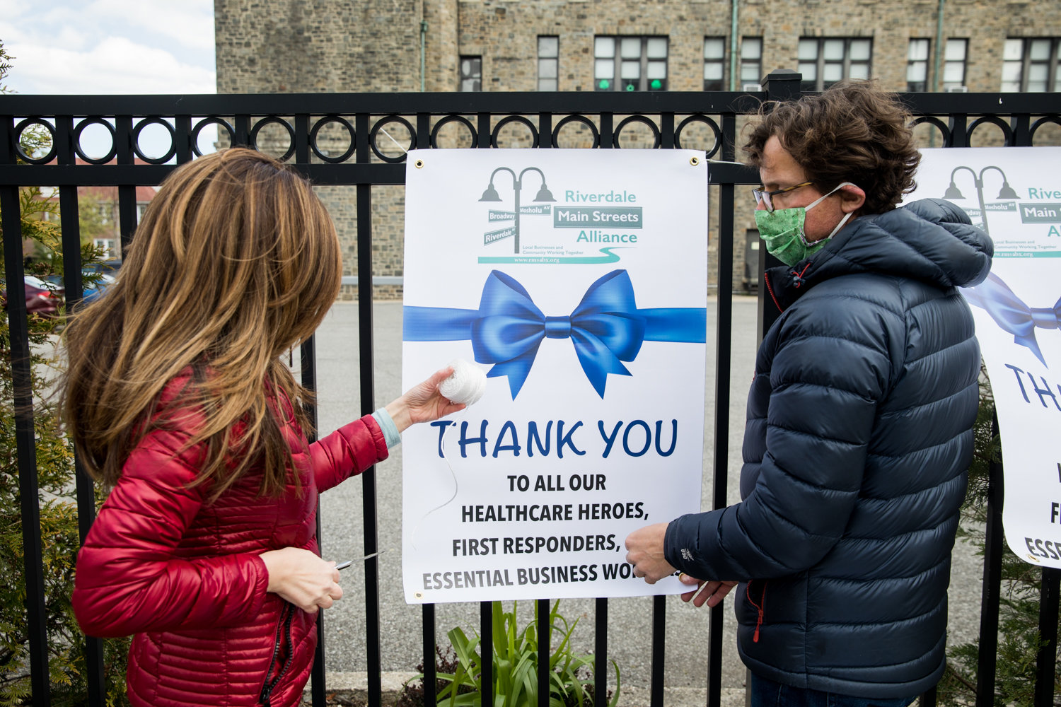 Giordana Avila and Christopher Rizzo hang signs thanking health care and essential workers on the fence outside St. Margaret of Cortona School on Riverdale Avenue. The signs are a part of a thank you campaign by the Riverdale Main Streets Alliance.