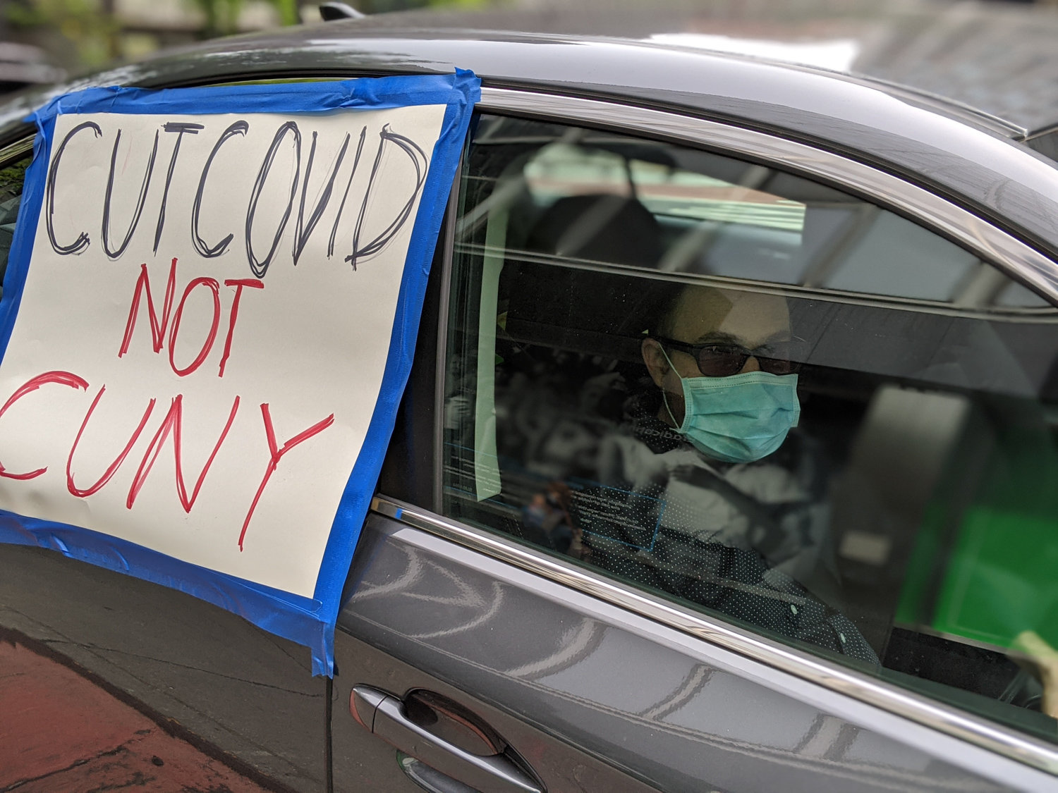 A sign that reads ‘cut COVID not CUNY’ is pasted on the window of a car during a protest organized by members of CUNY’s Professional Staff Congress. It was all in response to layoffs across the public university system — a consequence of the coronavirus pandemic.