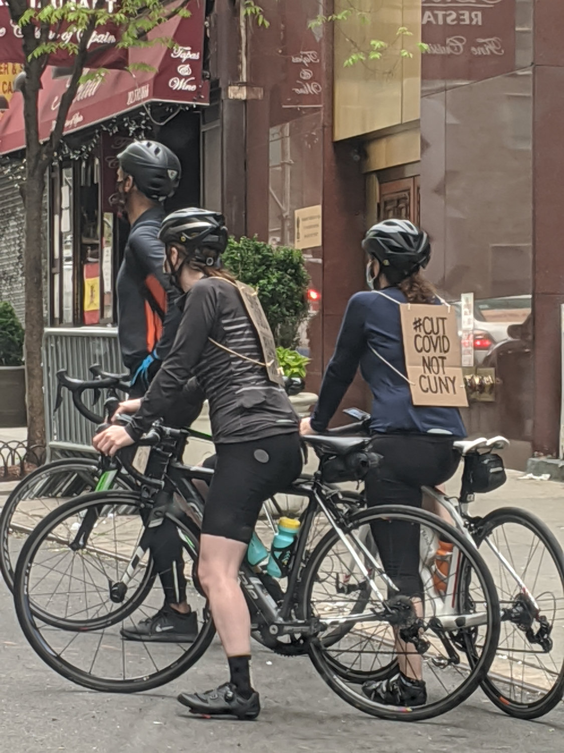 Cyclists wear cardboard signs during a protest against layoffs at various schools within the CUNY system.