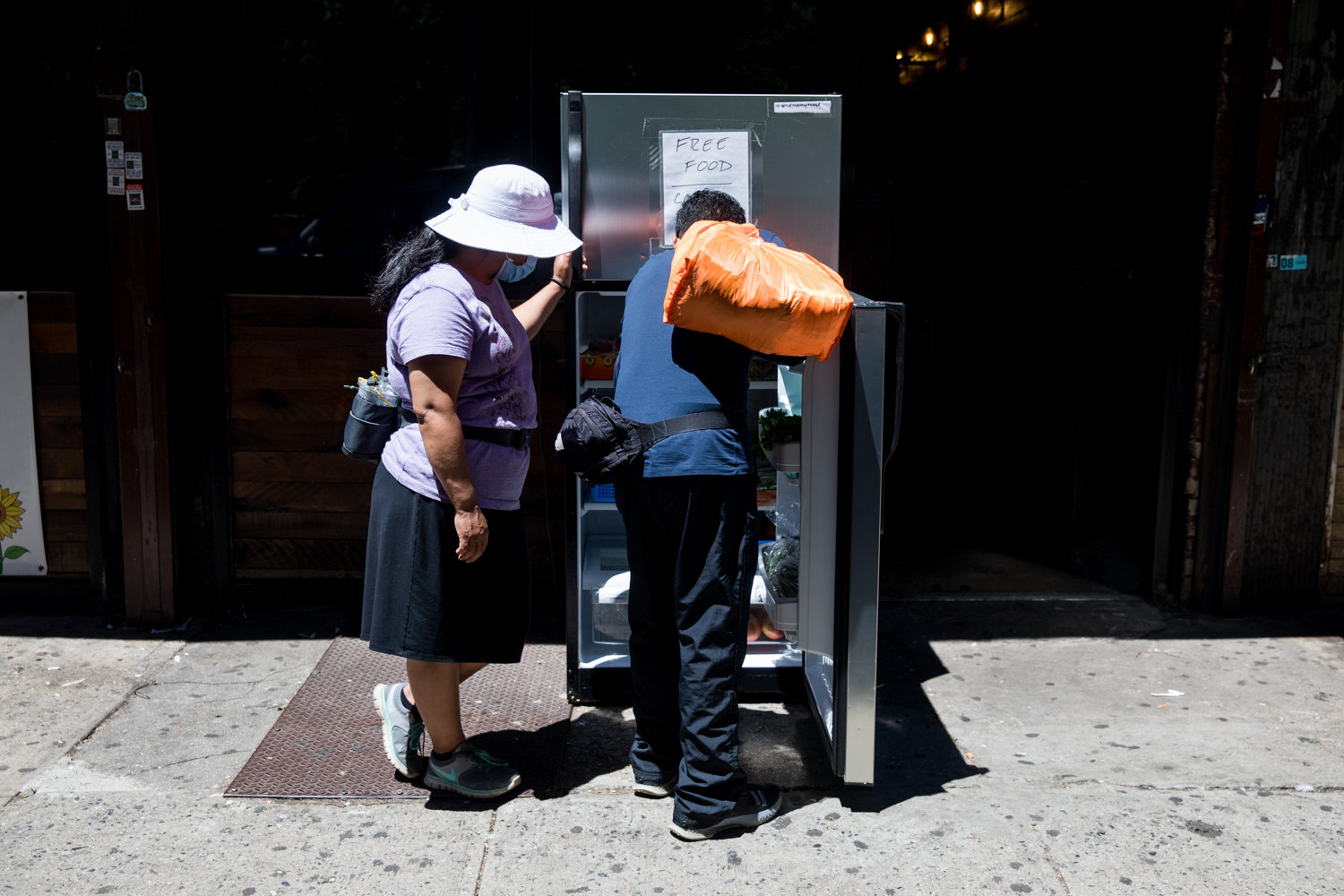 Passersby check a refrigerator outside The Last Stop on Broadway to see what food is available. The fridge there is part of a network across the city stocked by volunteers. Food is available for free to anyone who needs it.
