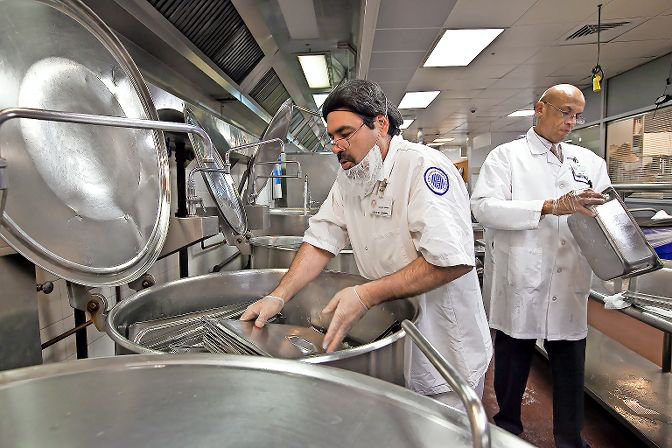 Harry Rivera places lids into a bath of steaming hot water as production manager Jerry Scott carefully inspects trays during kashering for Passover at the Hebrew Home at Riverdale in 2012. With some form of Seder returning this year in the wake of the coronavirus, preparing utensils for the holiday like this also returns to many homes and kosher eateries.