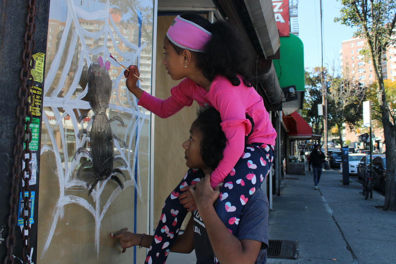 Kayla Perez, 17, and her sister Jayla, 8, paint a pink bow on their spider’s web on Johnson Avenue during the Halloween painting contest Saturday. Jayla was a winner.