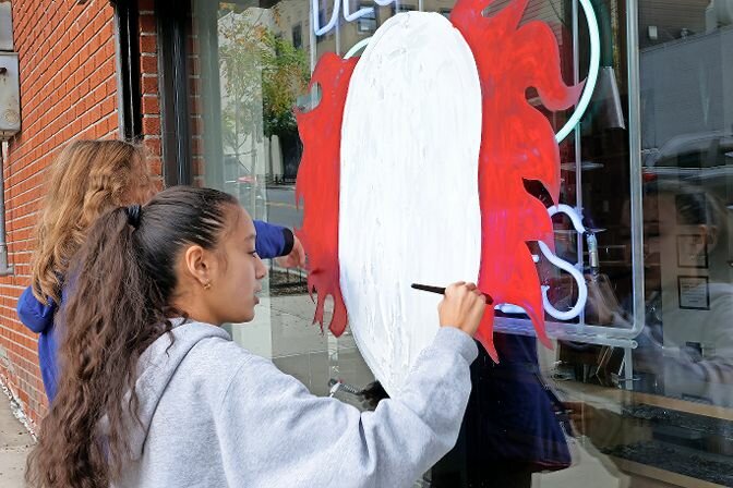 A girl paints the hair of a scary clown on the window of Steven John Opticians on Riverdale Avenue during Sunday's Halloween window painting contest.