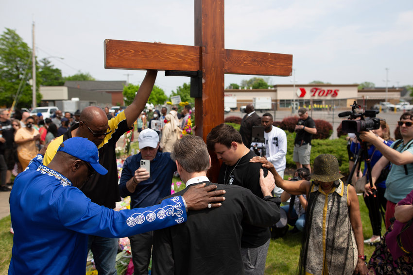 A group prays at the site of a memorial for the victims of the Buffalo supermarket shooting outside the Tops Friendly Market on Saturday, May 21, 2022, in Buffalo, N.Y.   Tops was encouraging people to join its stores in a moment of silence to honor the shooting victims Saturday at 2:30 p.m., the approximate time of the attack a week earlier. Buffalo Mayor Byron Brown also called for 123 seconds of silence from 2:28 p.m. to 2:31 p.m., followed by the ringing of church bells 13 times throughout the city to honor the 10 people killed and three wounded.