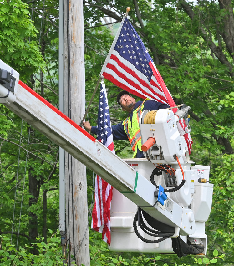 NEIGHBORLY ASSISTANCE &mdash;&nbsp;Chris Coleman, of the Rome Department of Public Works, places a flag on a utility post on Stokes-Westernville Road on Thursday. Each year the city of Rome helps out the hamlet of Westernville hang flags before Memorial Day weekend to help observe the solemn event and spread patriotic spirits.