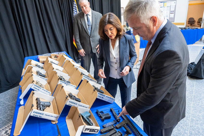 Gov. Kathy Hochul, center, and State Police Superintendent Kevin Bruen look over some of the dozens of guns seized by state police on Thursday during a press conference to discuss efforts to fight gun trafficking and crime in New York.