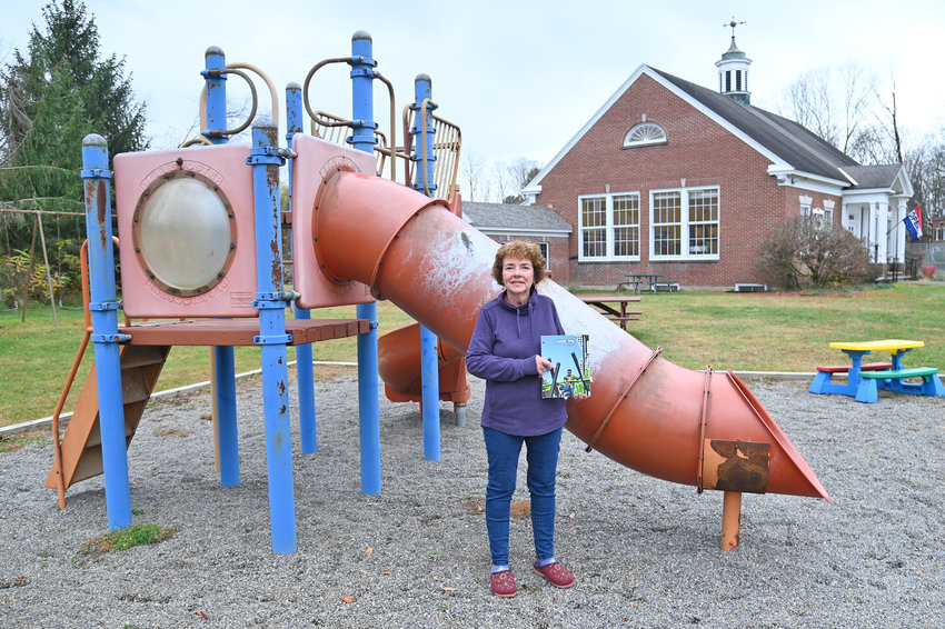 Jamie Wilbert poses Tuesday, Nov. 1 with the old playground equipment at the Western Town Library. She&rsquo;s holding a catalogue GameTime that will supply the new playground equipment.