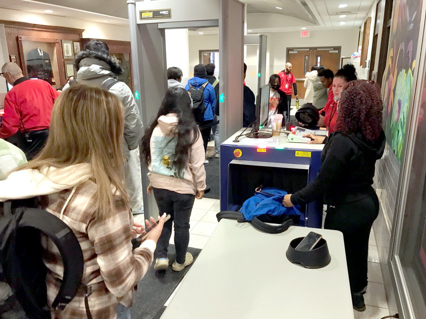 Proctor High School students put their backpacks and items from their pockets on a table Thursday, Dec. 1, to send through the bag scanner on the right before walking through a standup weapon detector unit on the left.