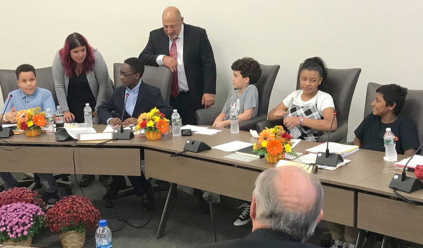 Kernan Elementary School Sixth Grade Student Council members, seated from left, Ivan Toledo, Nuer Gaw, Florentino Gonzalez, Jayrra Majias and Ikhram Hussaim chat with Utica City School District Board of Eduction Vice President Danielle Padula, standing left, and President Joseph Hobika Jr. at the board&rsquo;s October 2022 meeting.