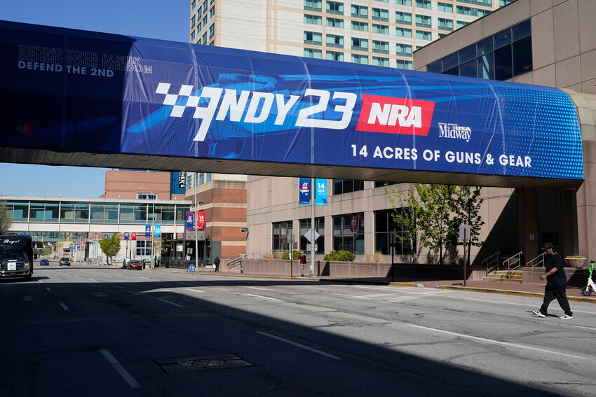 A pedestrian walks under a sign advertising the NRA Convention, Thursday, April 13, in Indianapolis. The convention began Friday, April 14, and ends Sunday, April 16.