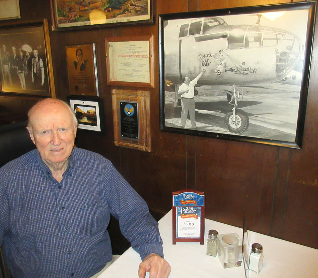 ROSIE’S RAT RACE — Former Air Force graphic artist Charlie Pfrimmer sits in the Savoy Restaurant by a photo of a B-25 which he decorated. In the picture, former Savoy owner Rosie Destito points to the artwork which was dedicated to him and the chariot races that were once held at the Beeches. Pfrimmer mad a series of paintings when he worked as an illustrator at Griffiss Air Force Base in the early 1950’s.
 (Sentinel photo by Roger Seibert)